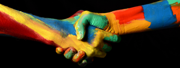 Two hands, each colorfully painted in oranges, blues, reds and greens, shaking hands.