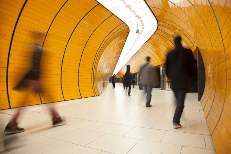 A blurry image of business people walking briskly through an orange hallway